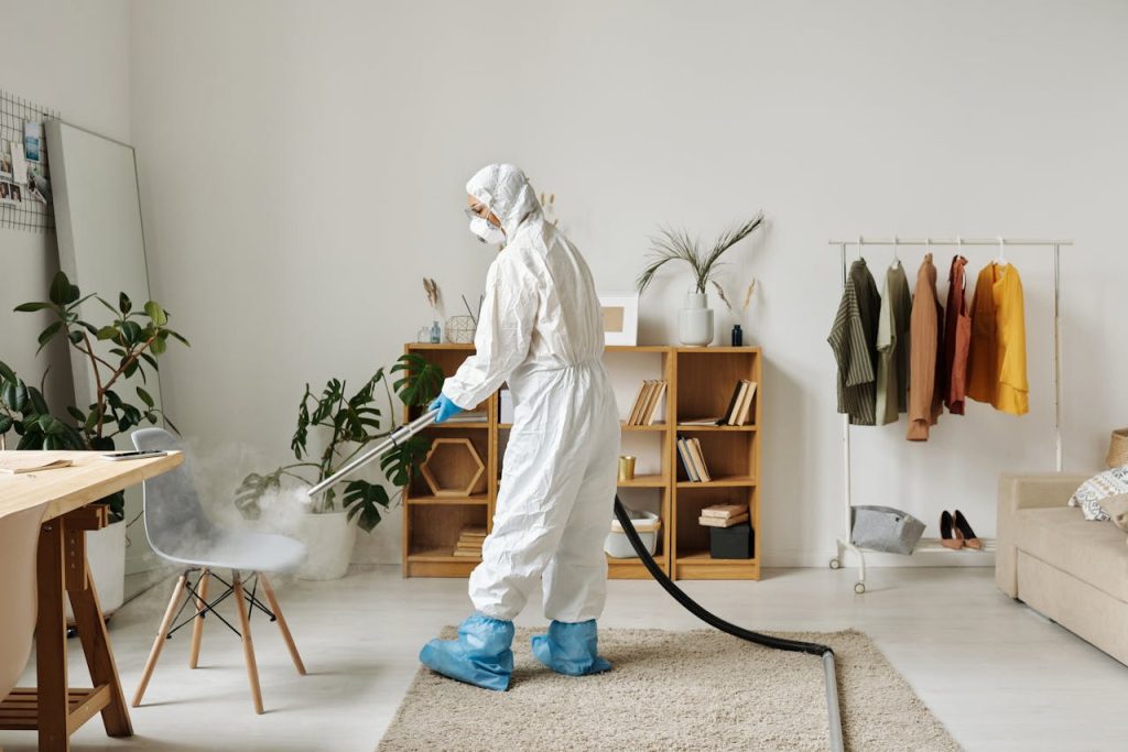 A worker in protective gear disinfecting a modern living room with a fogger.